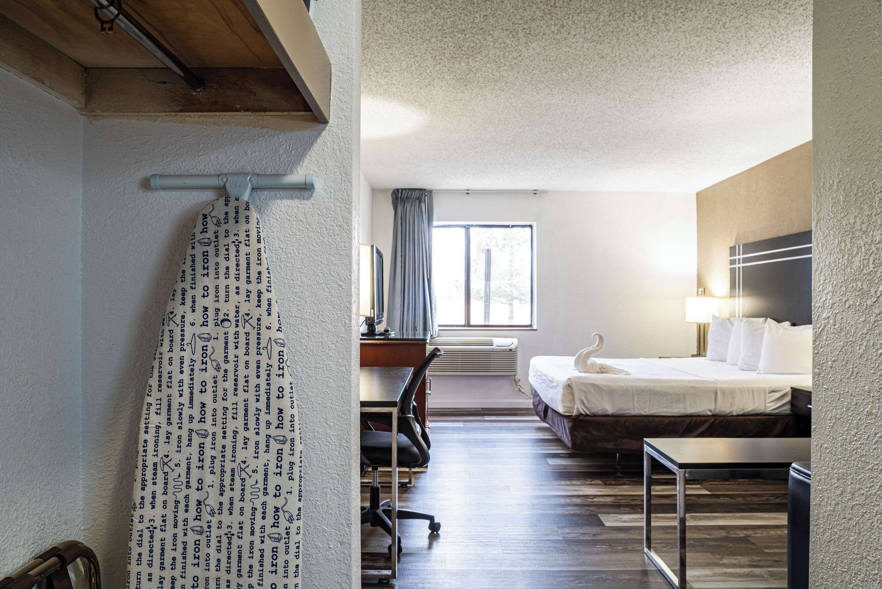 A hotel room with a bed, desk, chair, and a large window with curtains.