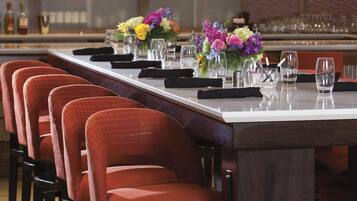 A bar area with a long counter, multiple bar stools, and a television mounted on the wall.
