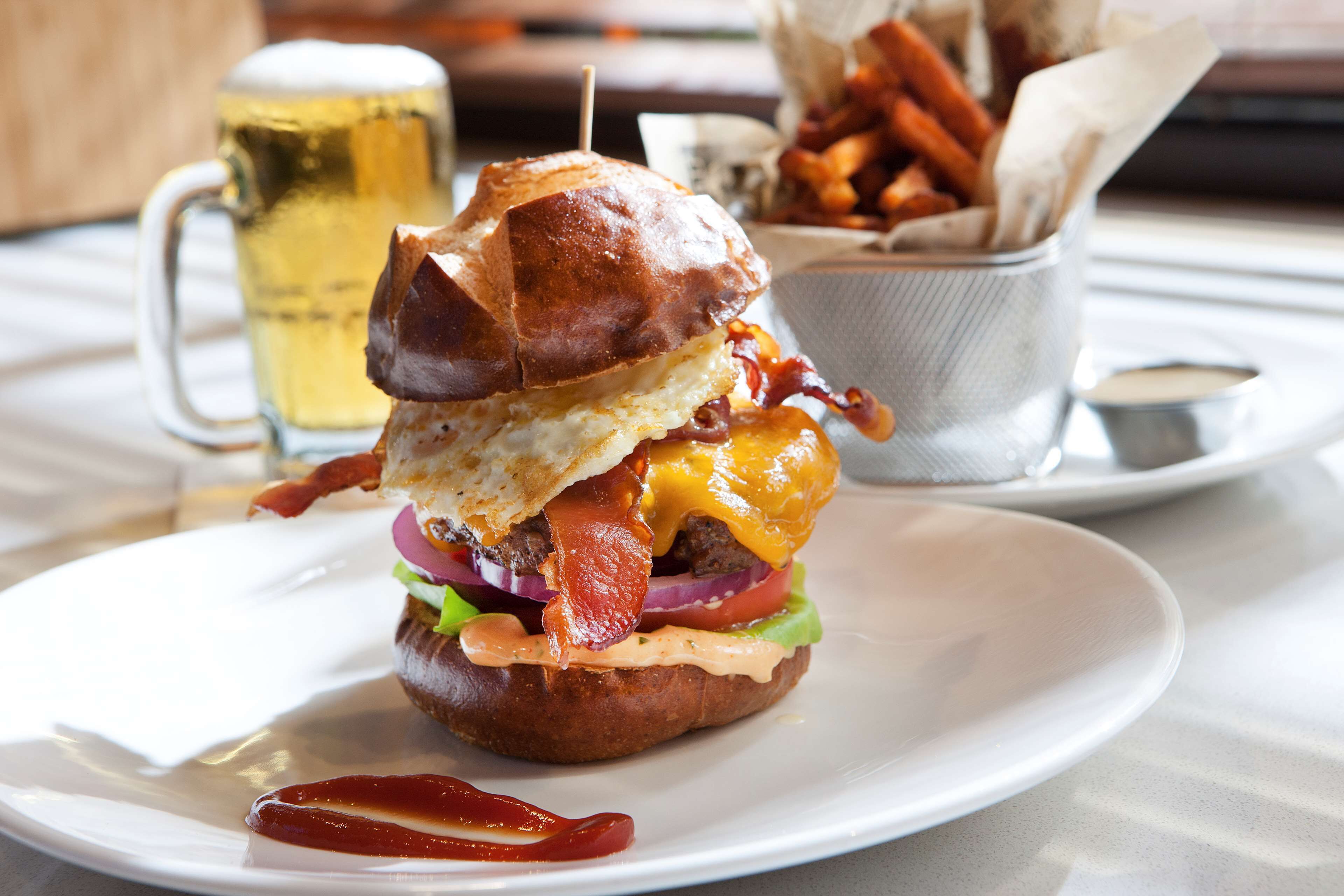 Ein Burger mit Speck, Käse und Salat auf einem weißen Teller.