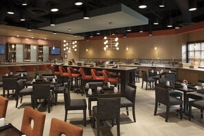 A modern restaurant with multiple seating areas, including booths and tables, and a bar counter with a variety of beverages.