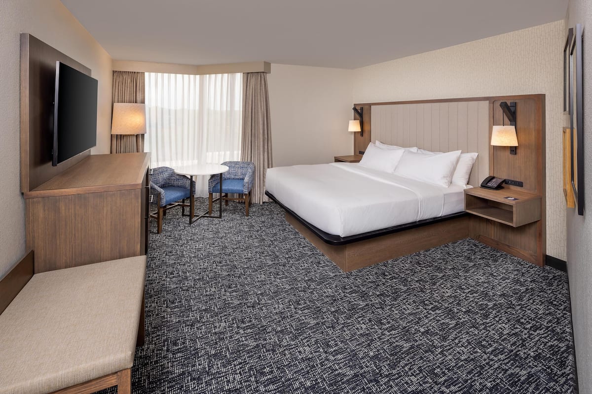 A hotel room with a bed, a desk with a chair, a TV, and a lamp.