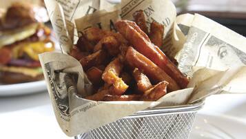 Uma cesta de batatas fritas em recipiente de malha, forrada com jornal, sobre um prato branco.