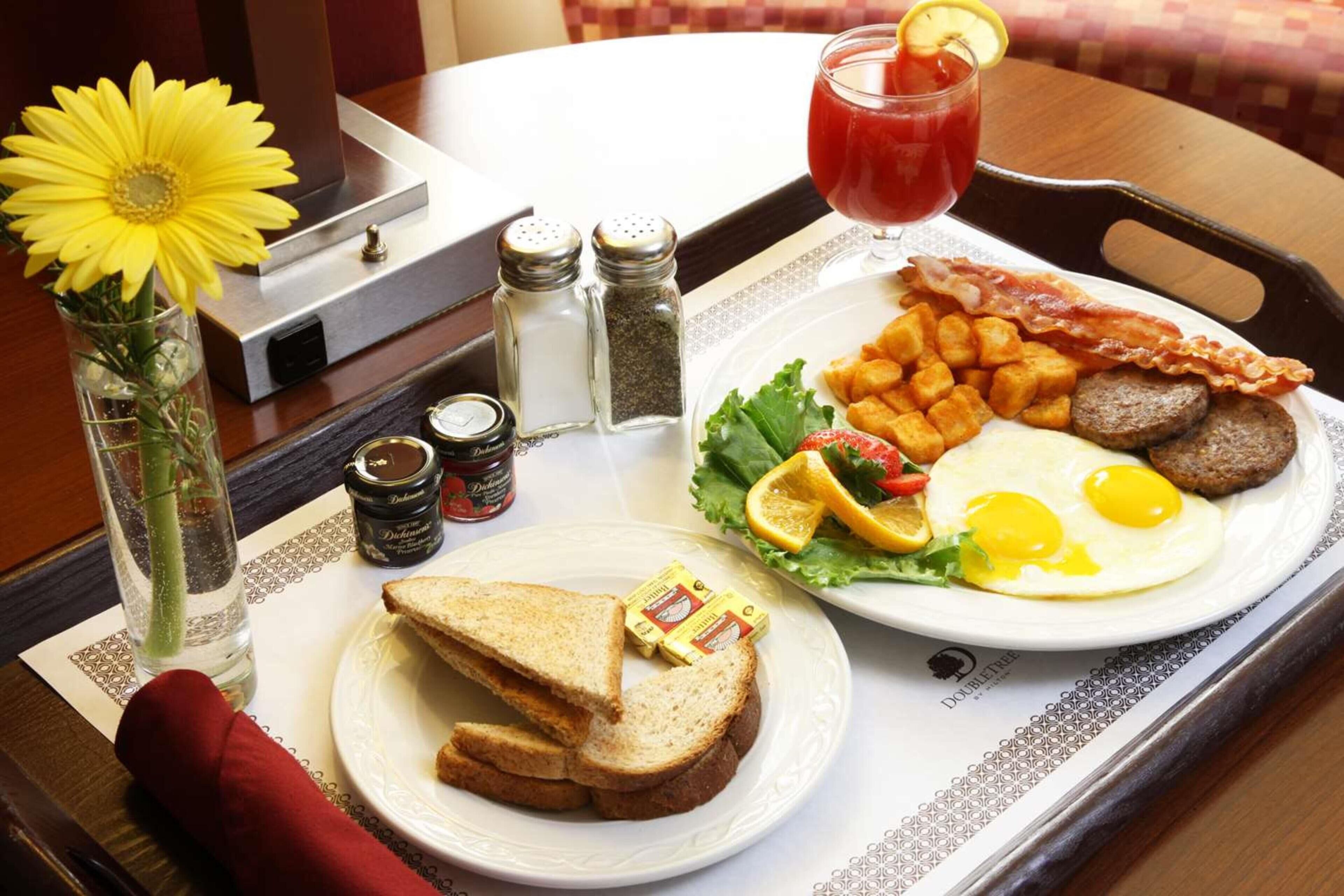 A breakfast tray with toast, eggs, bacon, sausages, and a drink.