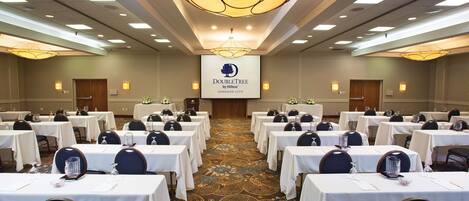 A conference room with rows of tables and chairs, a large screen displaying the DoubleTree logo, and a carpeted floor.