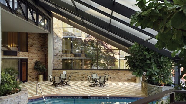 Una piscina interior con suelo a cuadros, rodeada de paredes de ladrillo y grandes ventanales.