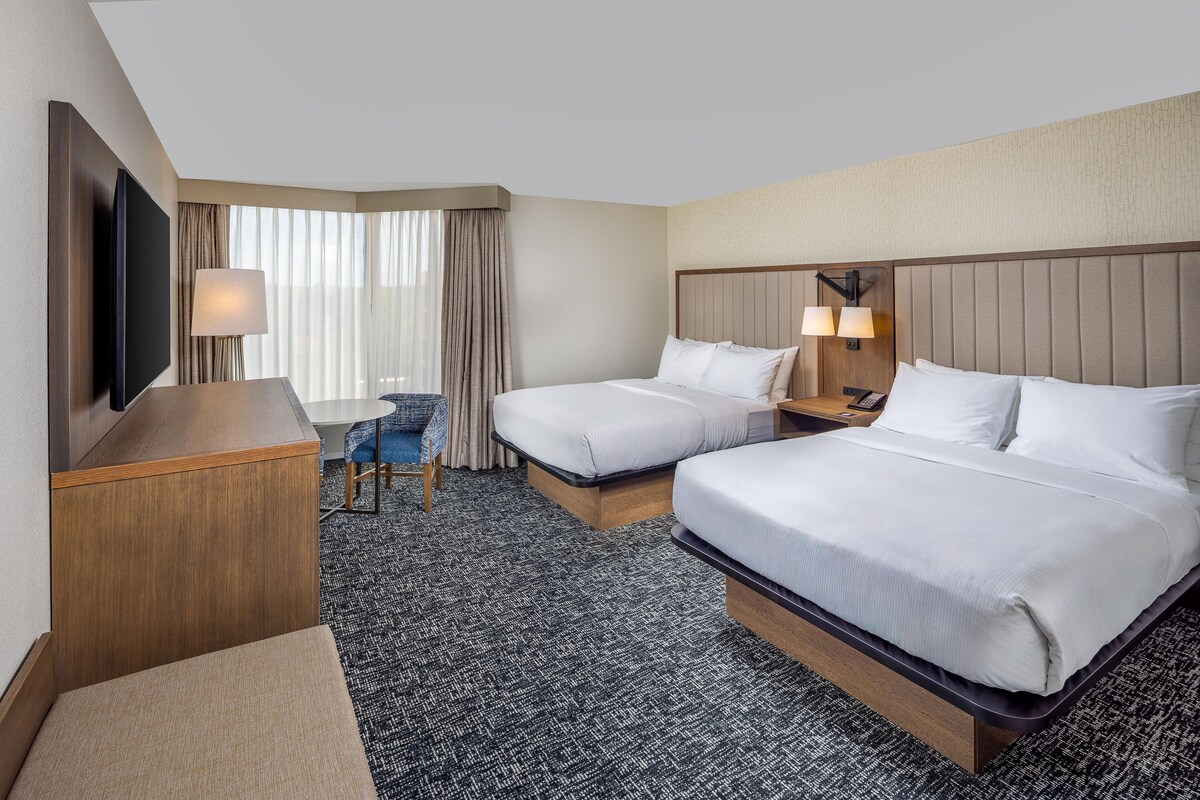 A hotel room with two beds, a desk, a TV, and a chair.
