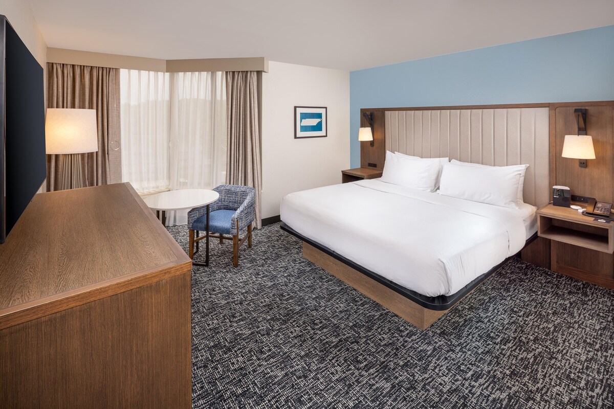 A hotel room with a large bed, a desk, a chair, and a TV.
