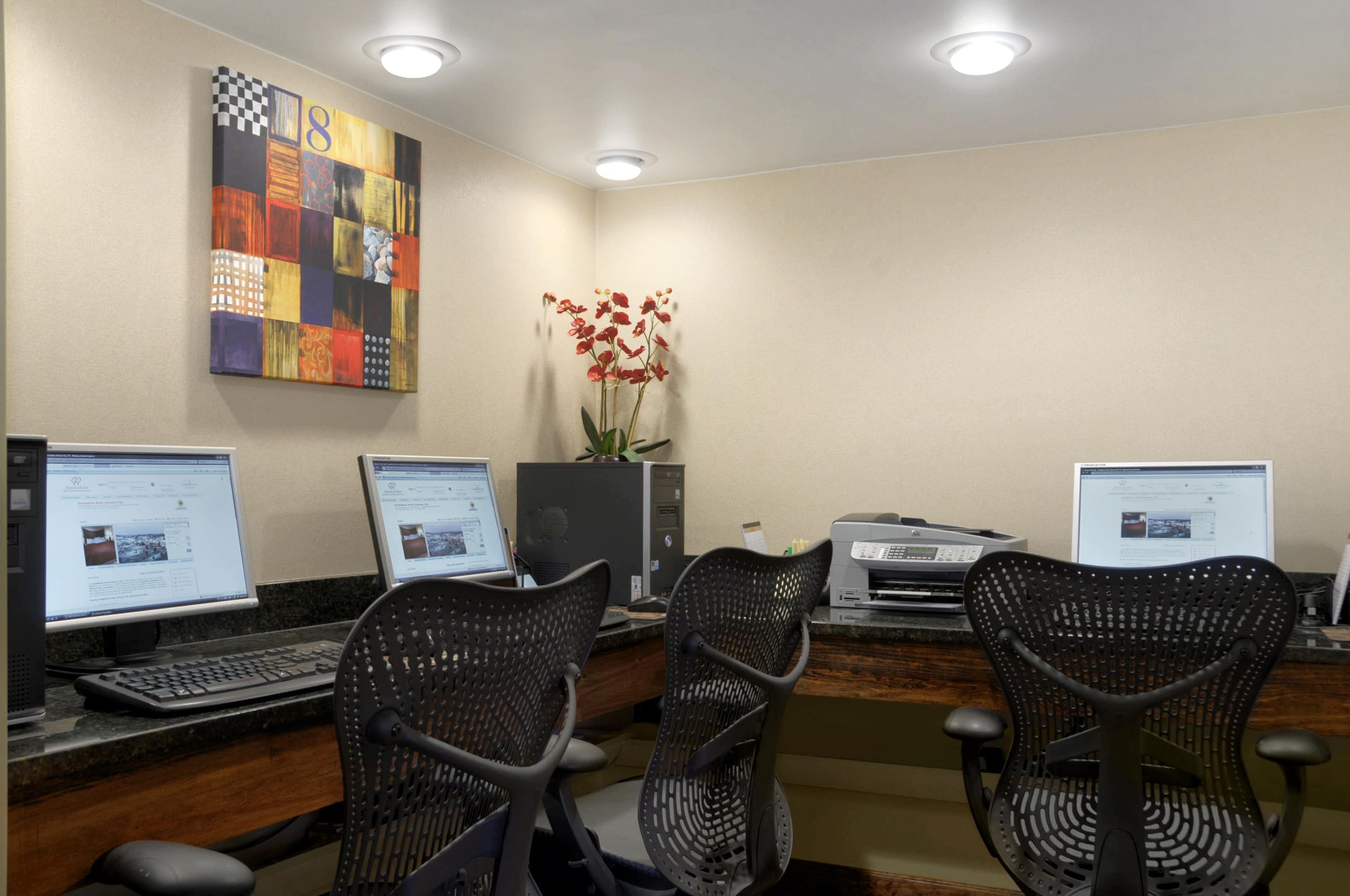 Un laboratorio de computación con tres estaciones de trabajo, cada una con monitor, teclado y una silla de oficina negra con perforaciones.
