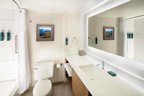 A modern bathroom with a toilet, sink, and shower. There are framed pictures on the wall, a towel rack, and toiletries on the sink.