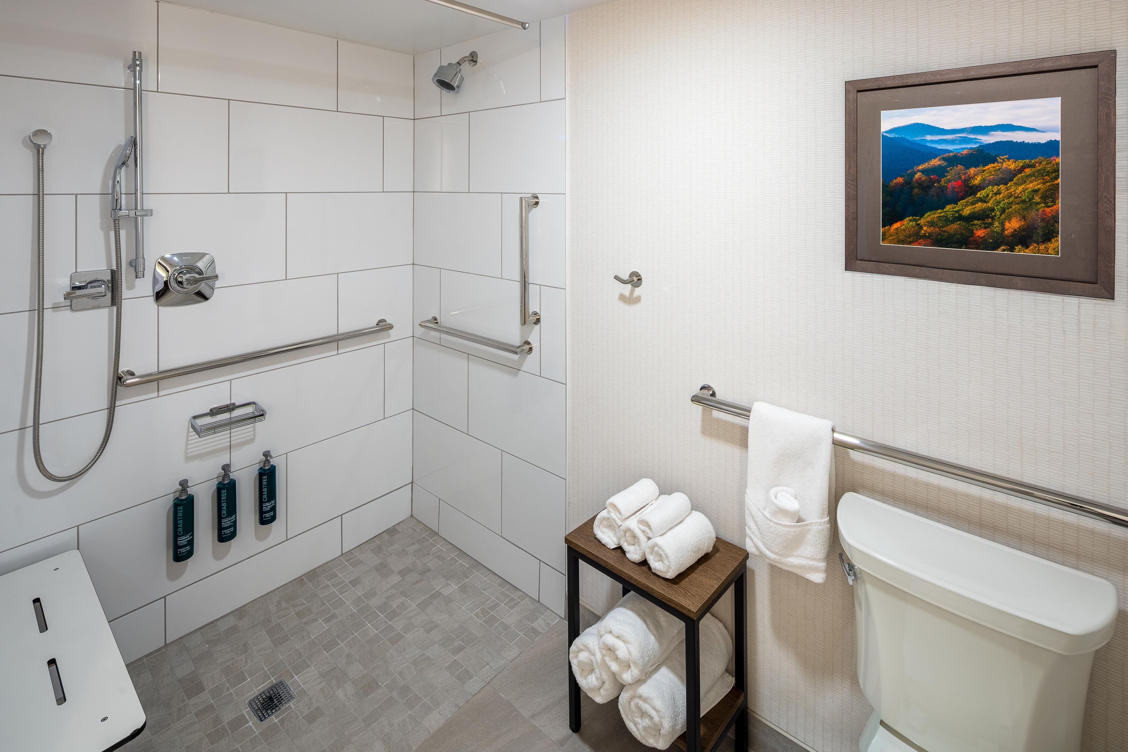 A bathroom with a shower, toilet, and a small table with towels.