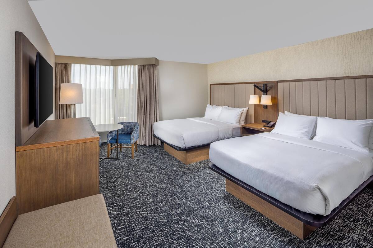 A hotel room with two beds, a desk, a TV, and a chair.