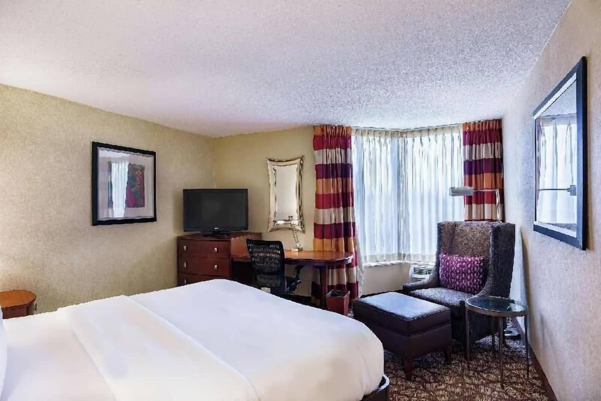 A hotel room with a bed, a desk, a chair, a television, and a window with curtains.