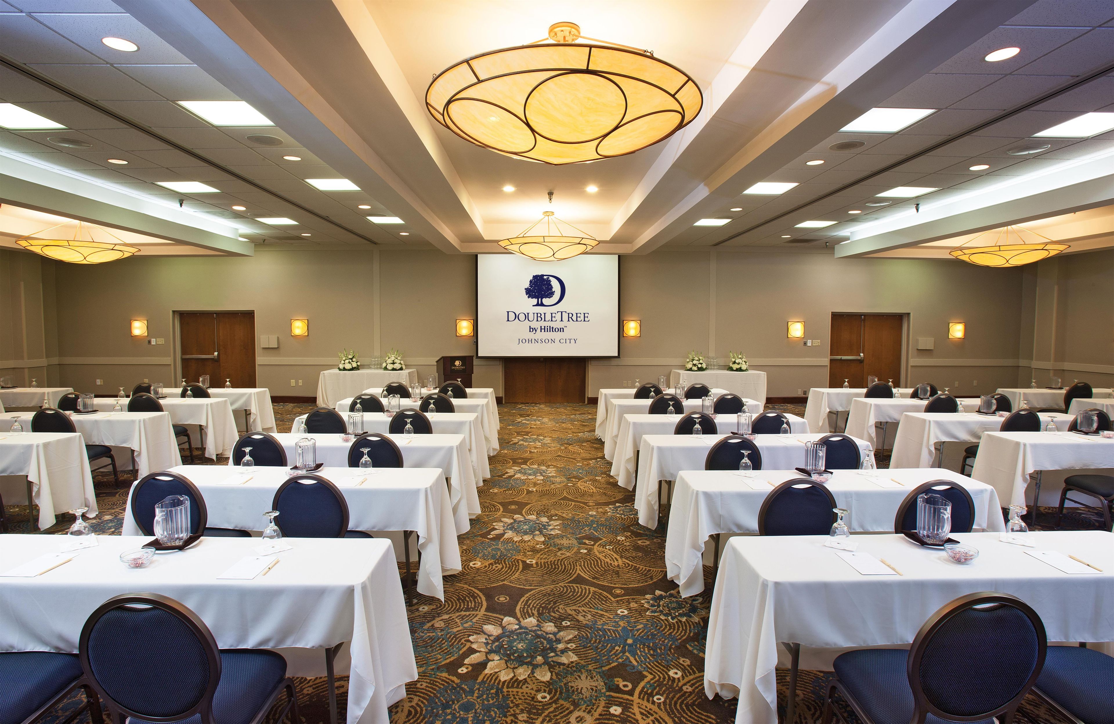 A conference room with tables, chairs, and a large screen displaying the hotel name.