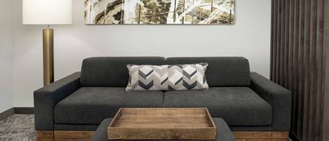 Una sala de estar moderna con un sofá gris, una mesa de centro de madera, un cojín estampado, una lámpara de pie y un cuadro abstracto grande en la pared.