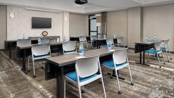 A conference room with tables and chairs, a flat-screen TV, and water bottles on the tables.
