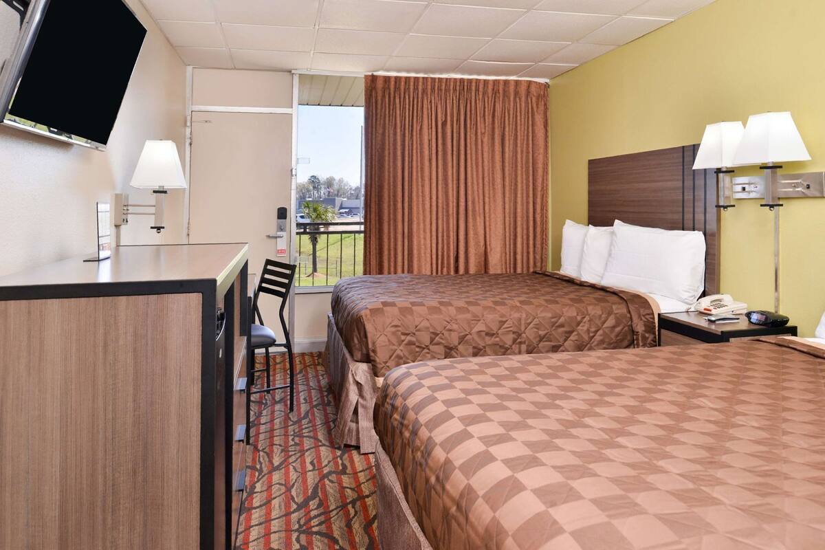 Een hotelkamer met twee bedden, een bureau, een stoel, een televisie en een raam met gordijnen.