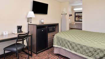 A hotel room with a bed, desk, chair, television, and a small refrigerator.
