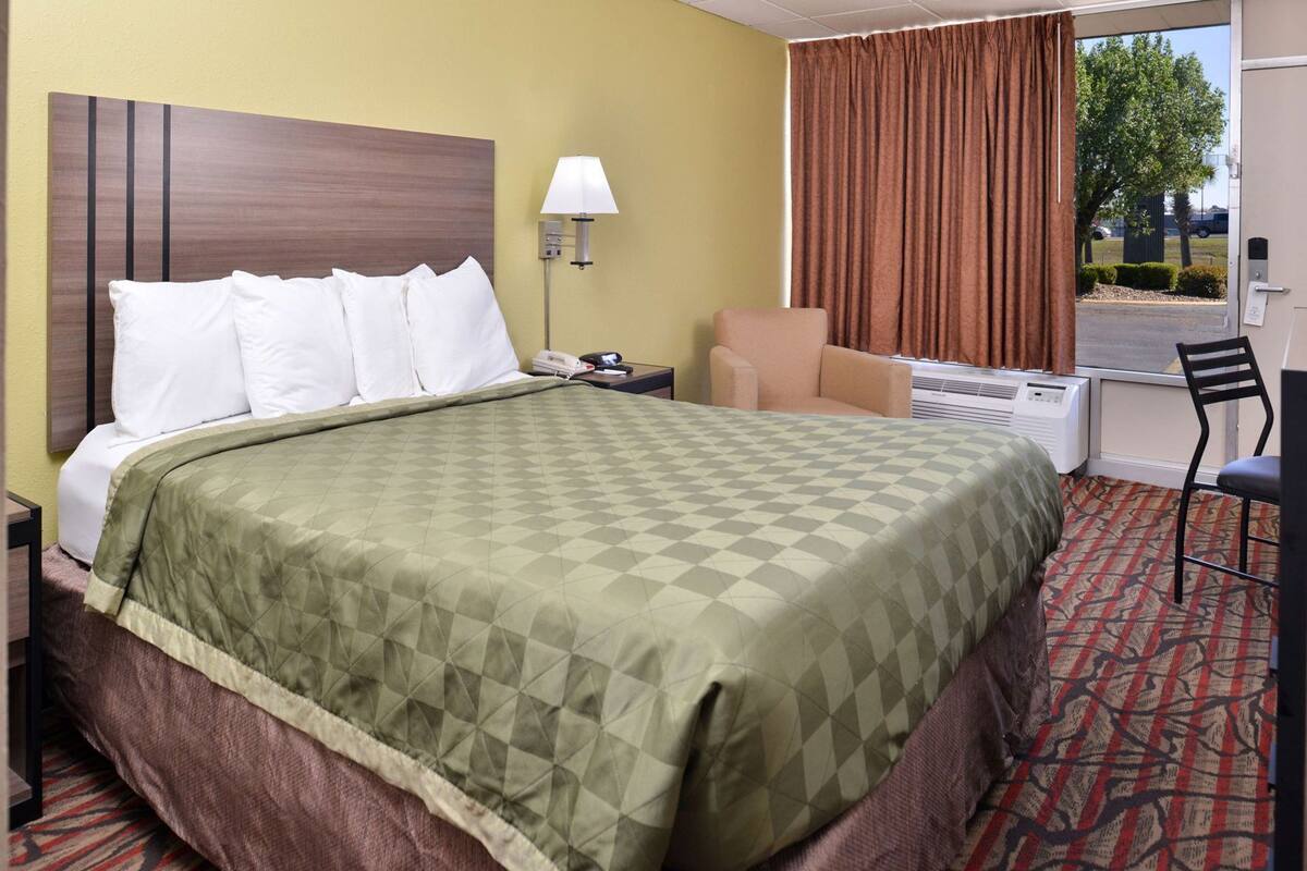 Een hotelkamer met een bed, een stoel, een bureau, een lamp en uitzicht op de omgeving.