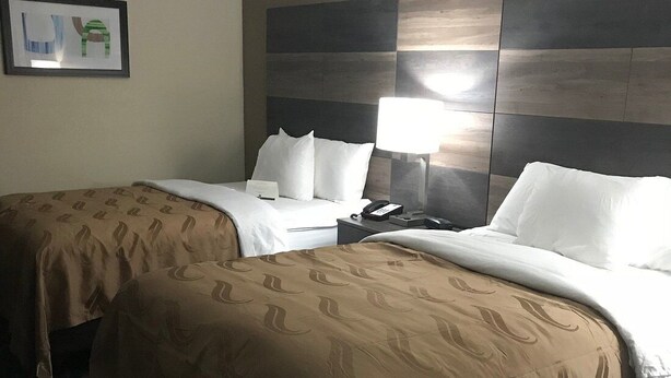 A hotel room with two beds, a nightstand, a lamp, and a framed picture on the wall. - Rodeway Inn Asheboro (Asheboro)
