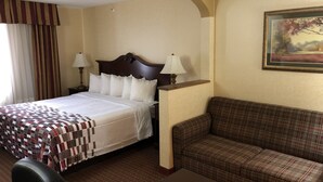 A hotel room with a bed, two bedside lamps, a couch, and a painting on the wall. - Red Roof Inn & Suites Chestertown (Chestertown)