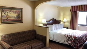 A hotel room with a bed, a sofa, a nightstand, a lamp, and a painting on the wall. - Red Roof Inn & Suites Chestertown (Chestertown)