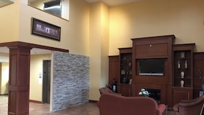 A spacious living room with a fireplace, a stone accent wall, and a television mounted above it. - Red Roof Inn & Suites Chestertown (Chestertown)