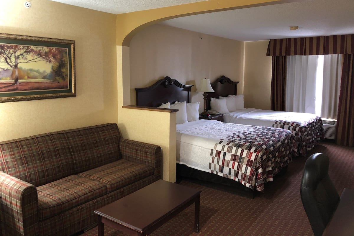 A hotel room with a sofa, two beds, a desk, and a painting on the wall.