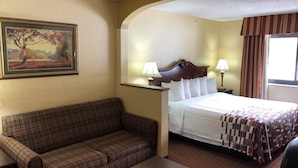 A hotel room with a bed, a couch, a painting, and a window with curtains. - Red Roof Inn & Suites Chestertown (Chestertown)