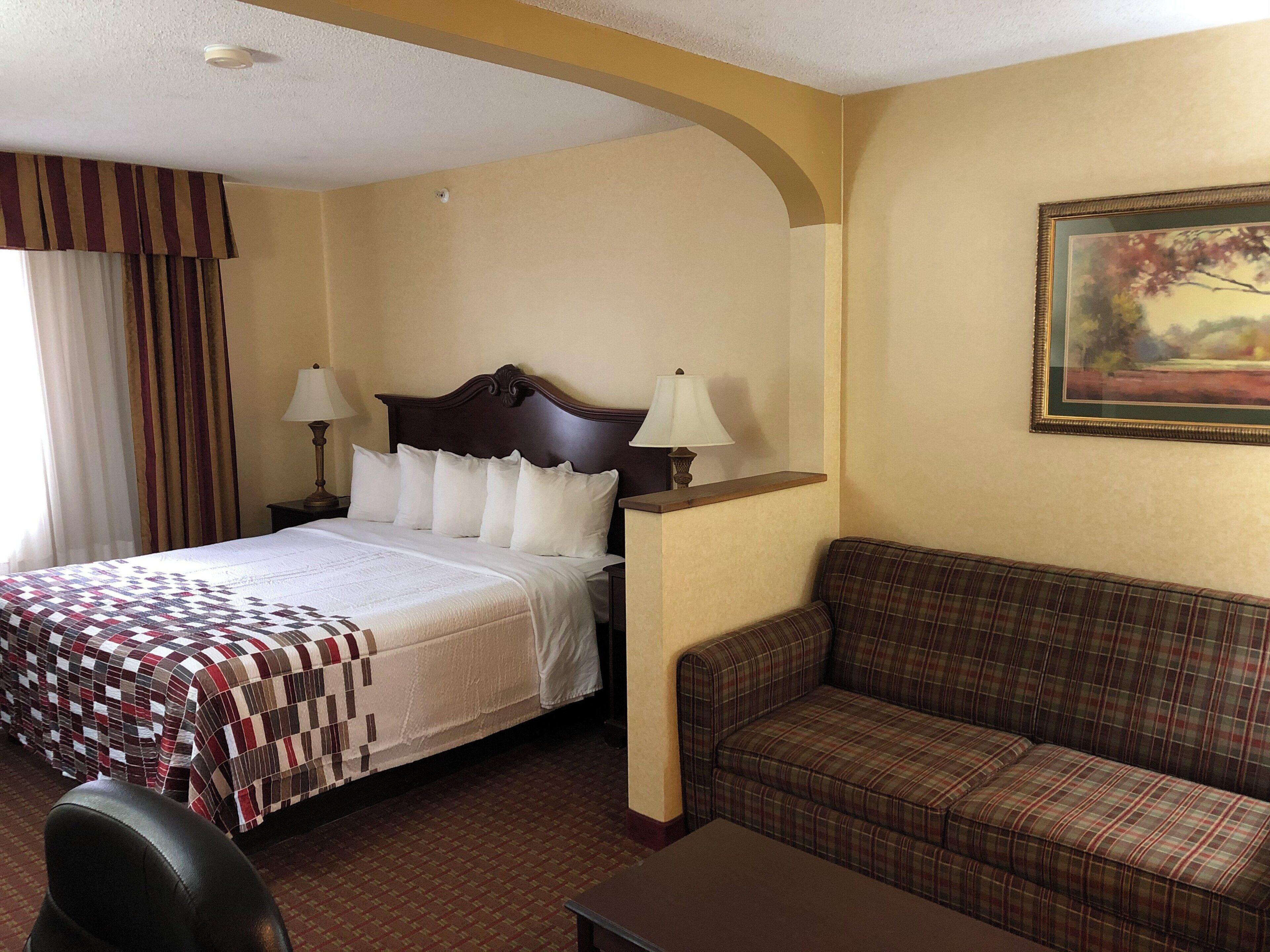 A hotel room with a bed, a sofa, a desk, and a painting on the wall.