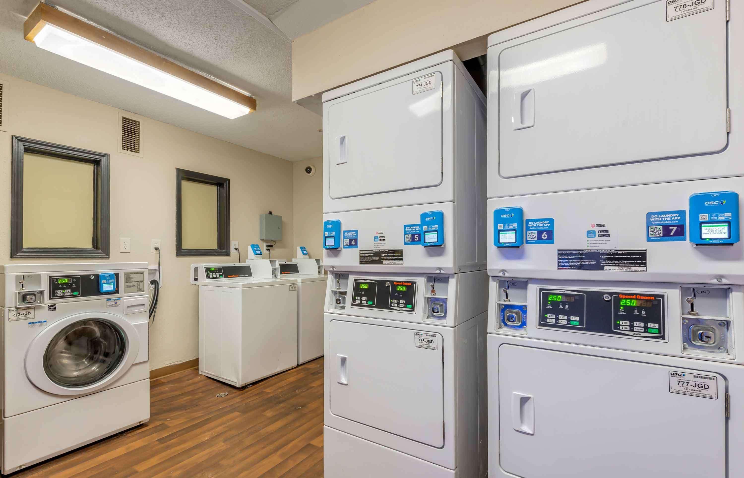 A laundry facility with multiple washing machines and dryers, control panels, and a ventilation system.