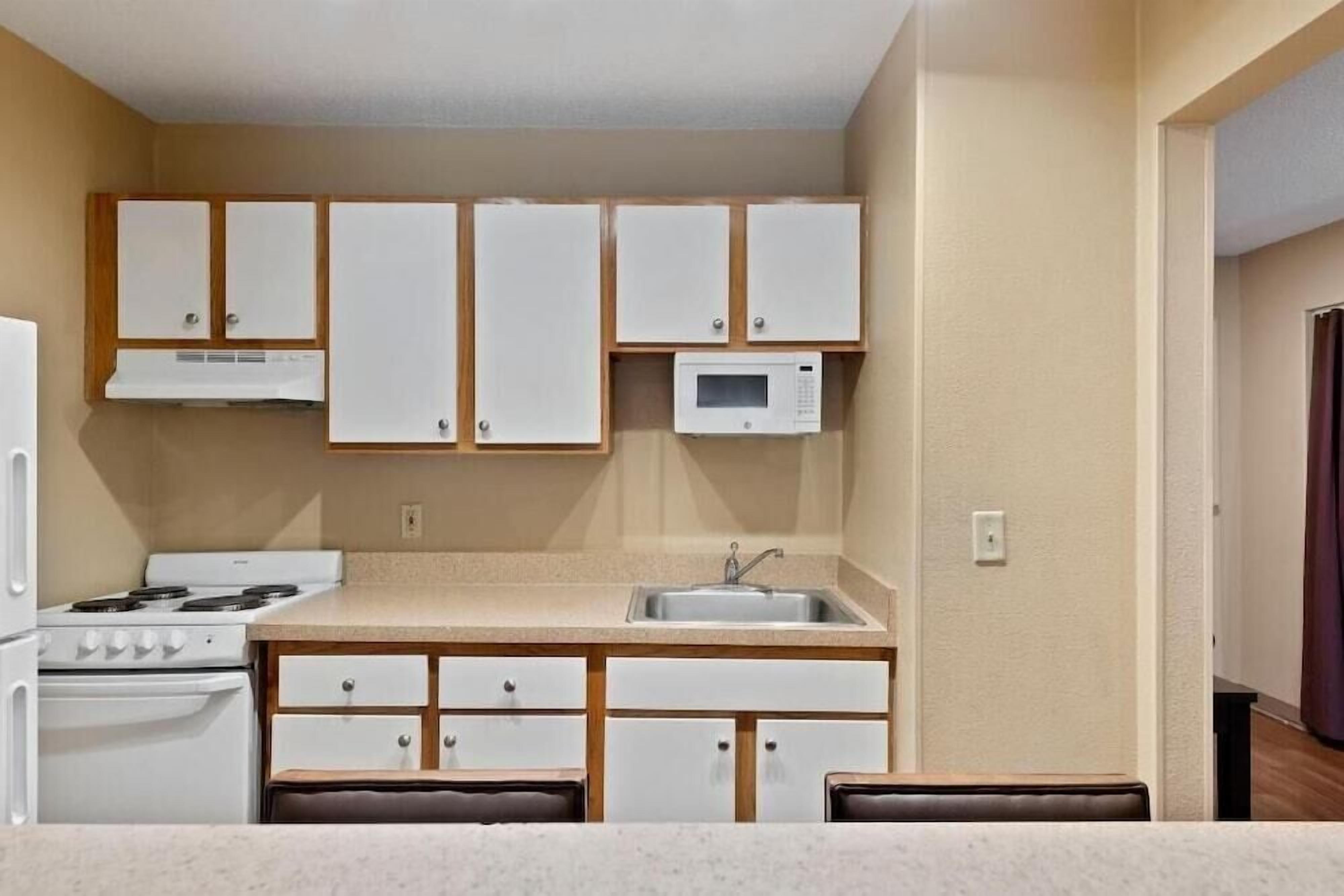A compact kitchen with white cabinets, a microwave, a stove, and a sink.