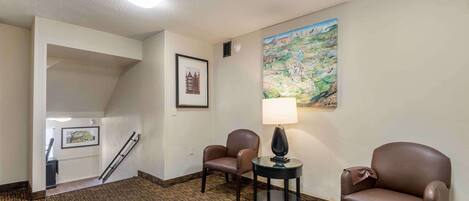Habitación de hotel con piso alfombrado, dos sillones de cuero, una mesita con lámpara, un cuadro en la pared y una escalera que conduce a otra habitación.