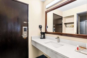 A bathroom with a dark wooden door, a white sink with a mirror above it, and a coffee maker on the counter.