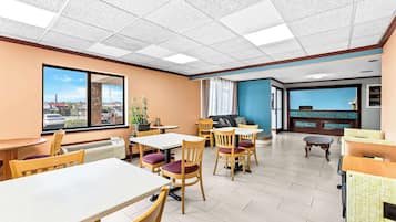 Un vestíbulo de hotel con varias zonas de estar, incluyendo mesas y sillas, un mostrador de recepción y vistas al exterior.
