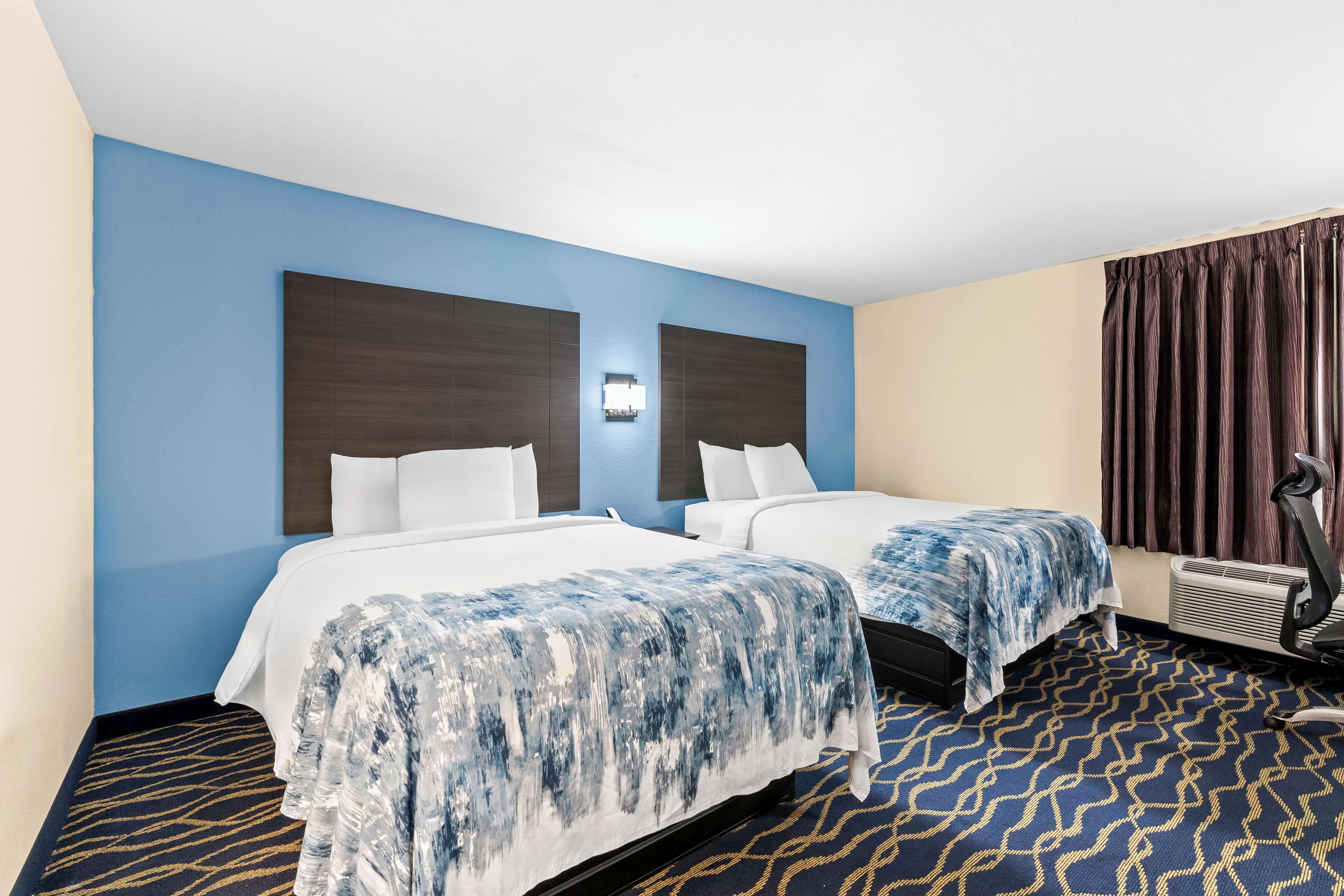 Habitación de hotel con dos camas, aire acondicionado de pared y alfombra estampada.