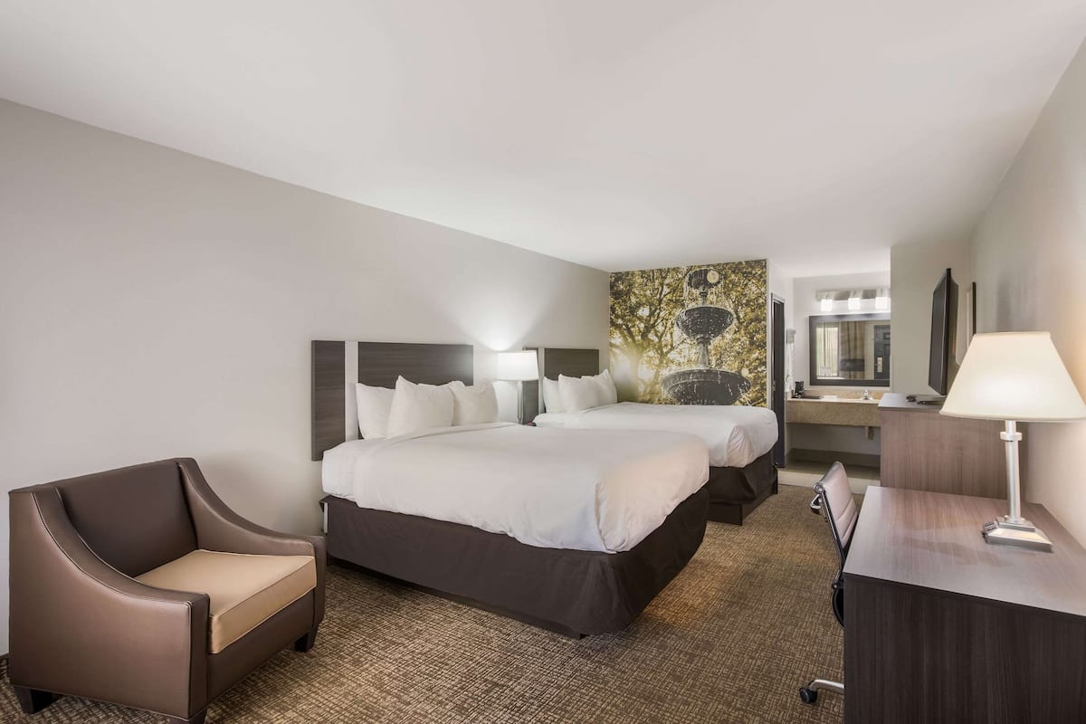 A hotel room with two beds, a desk, a chair, and a large mirror.