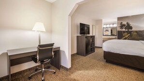 A hotel room with a desk, chair, bed, TV, and a bathroom with a mirror and sink. - Clarion pointe near I-75 (Forsyth)