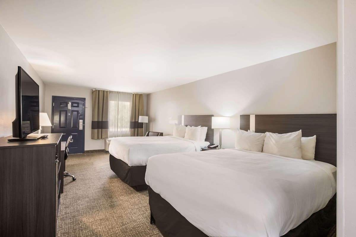 A hotel room with two beds, a desk, a TV, and a door.