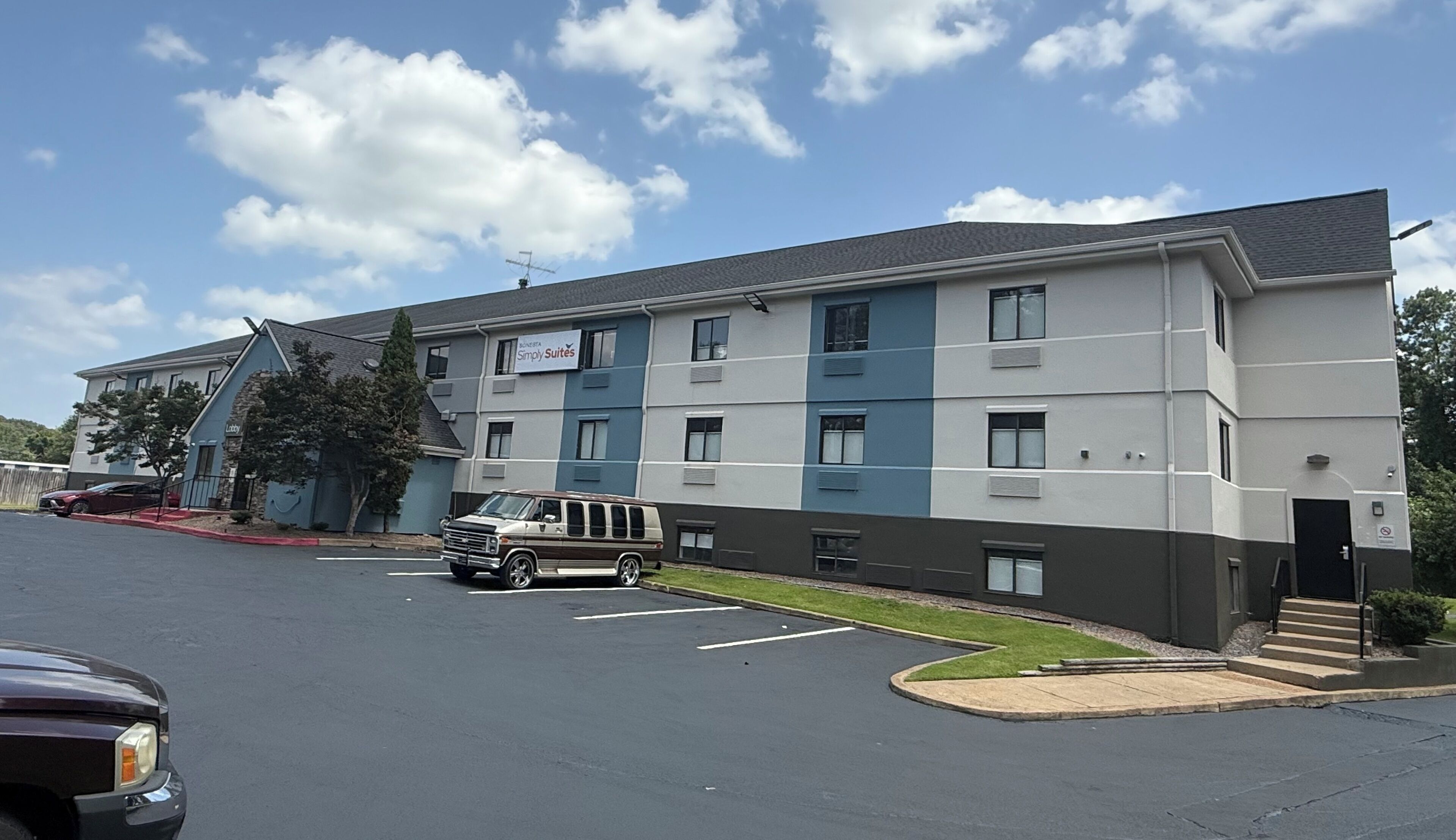 A multi-story hotel with a modern design, featuring a parking lot and a red vehicle parked in front.