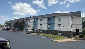 Un hôtel à plusieurs étages, doté d’un design moderne, comprenant un parking et un véhicule rouge garé devant l’entrée.