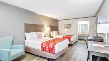 A hotel room with two beds, a desk, a chair, and a window.