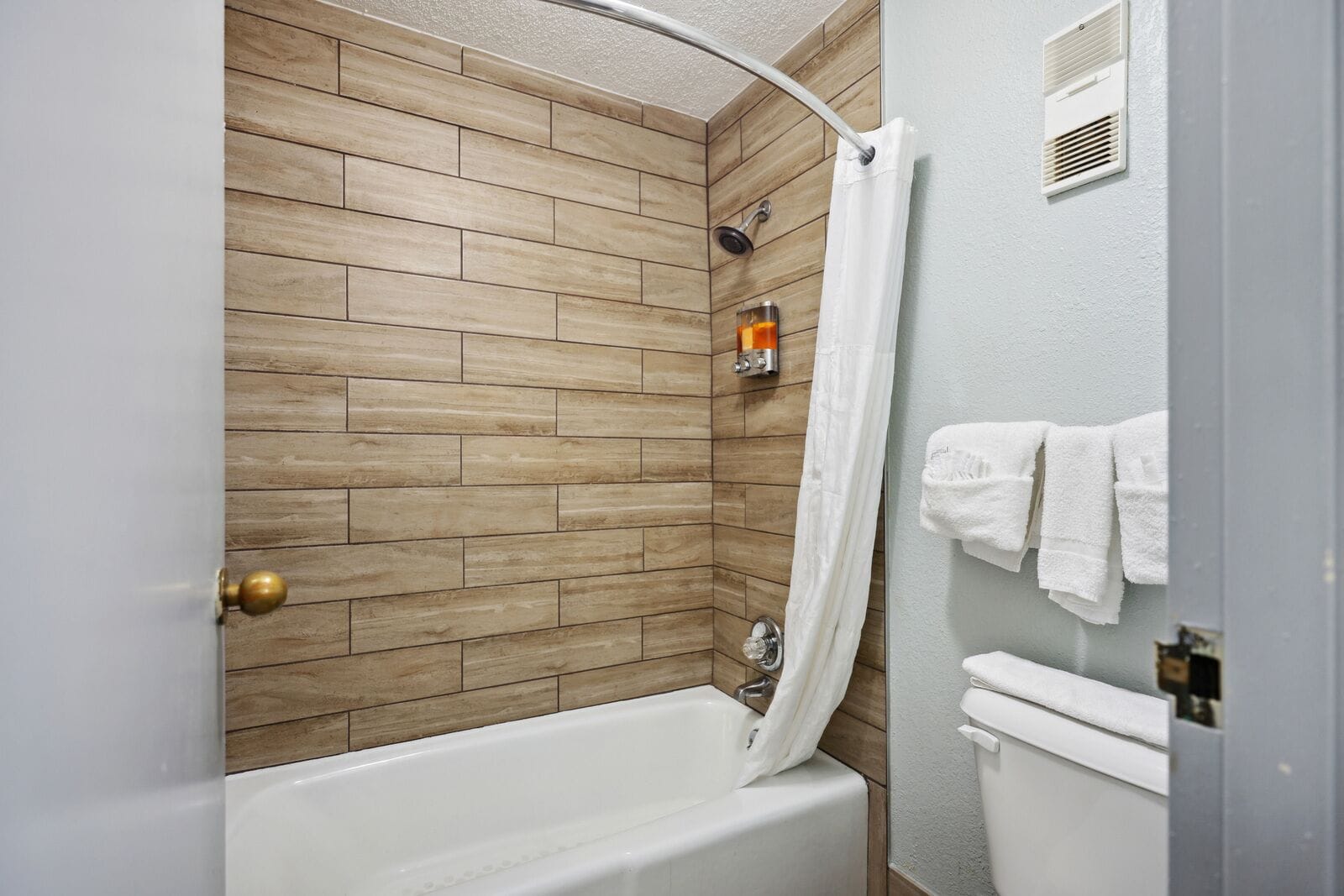 A bathroom with a wooden wall, a shower with a curtain, a bathtub, and a toilet with towels.