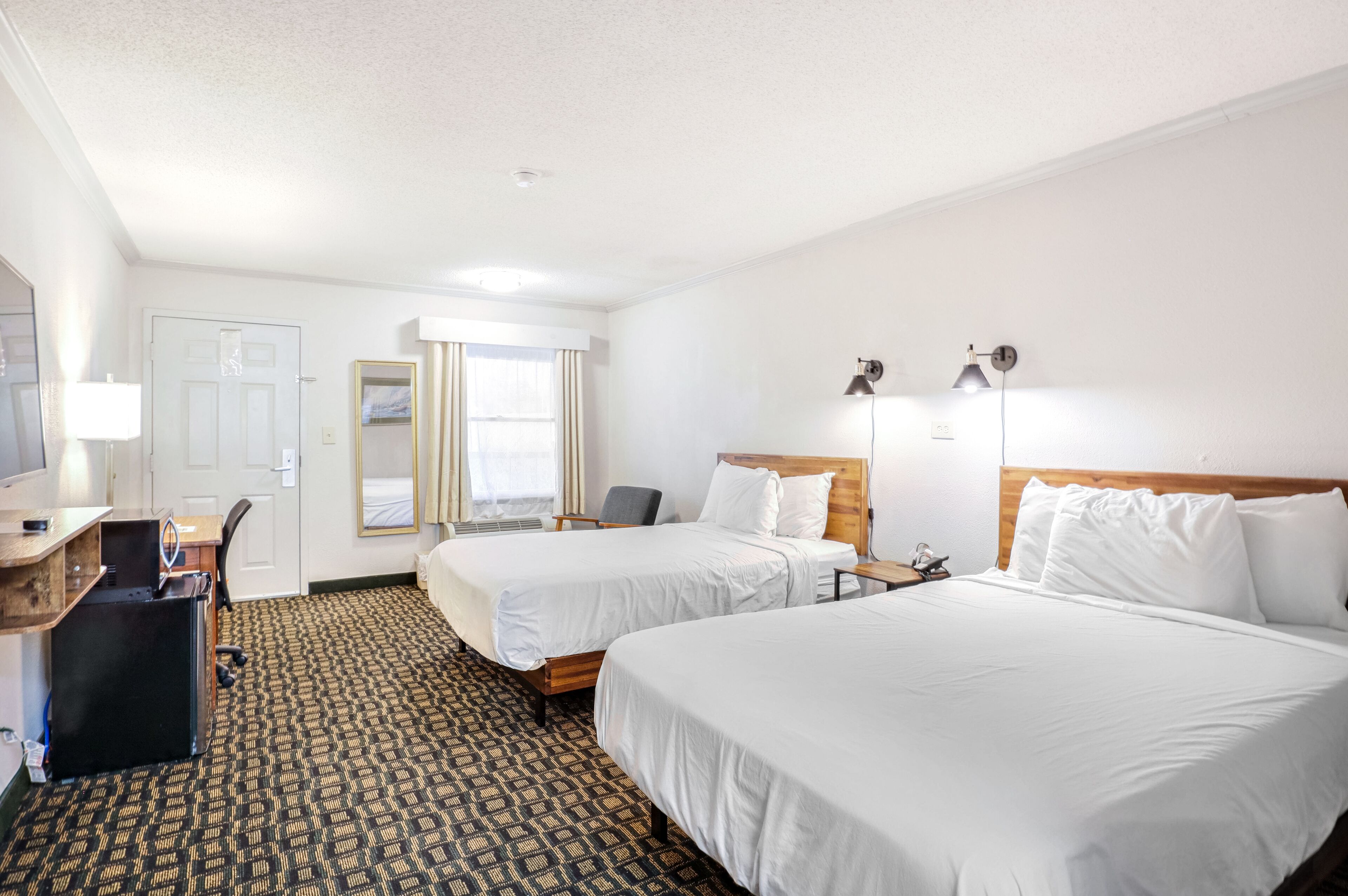 A hotel room with two beds, a desk with a computer, a chair, and a lamp.