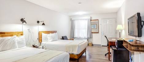 A hotel room with two beds, a desk, a chair, a television, and a window with curtains.