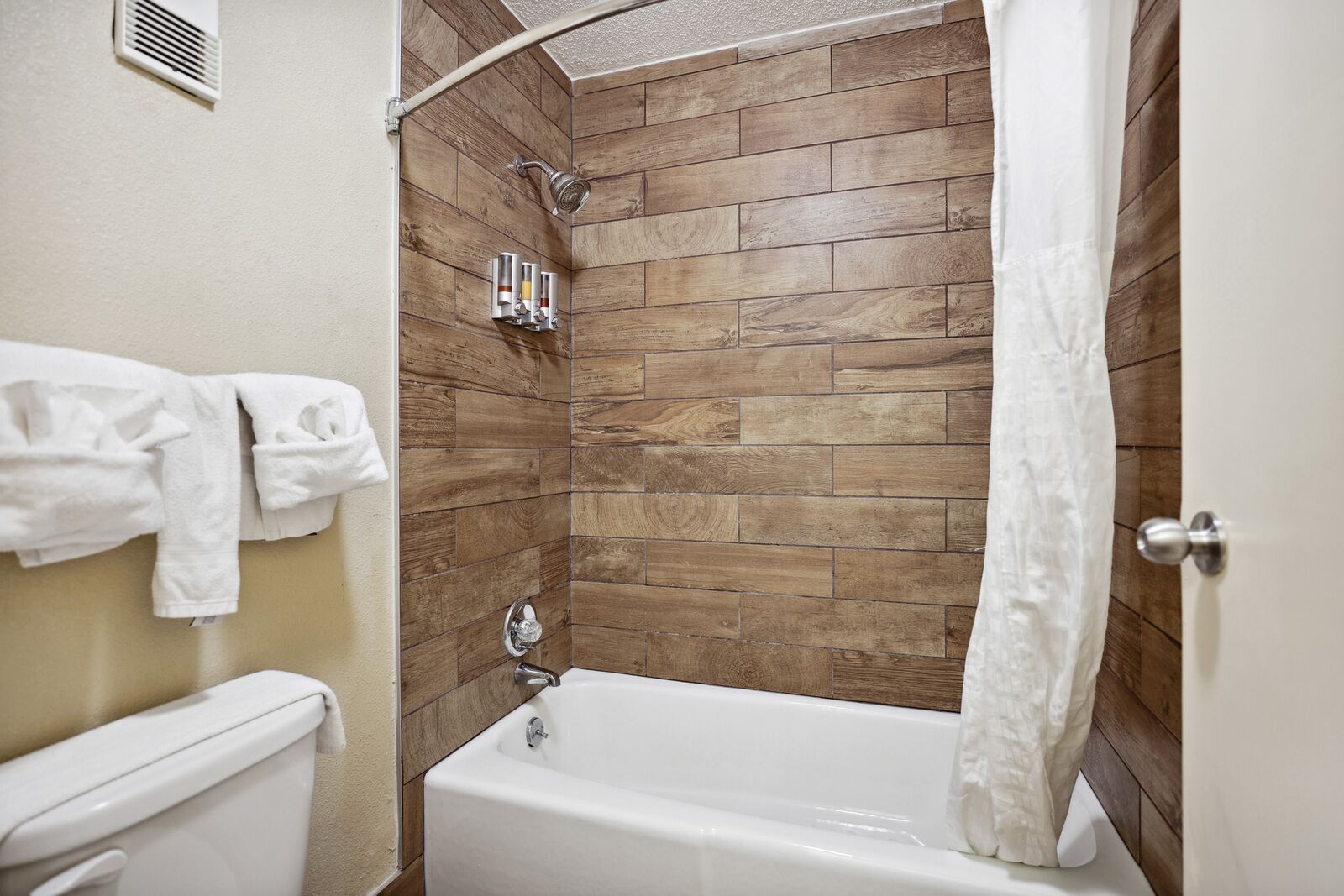 Un baño con pared de madera, bañera, ducha e inodoro.