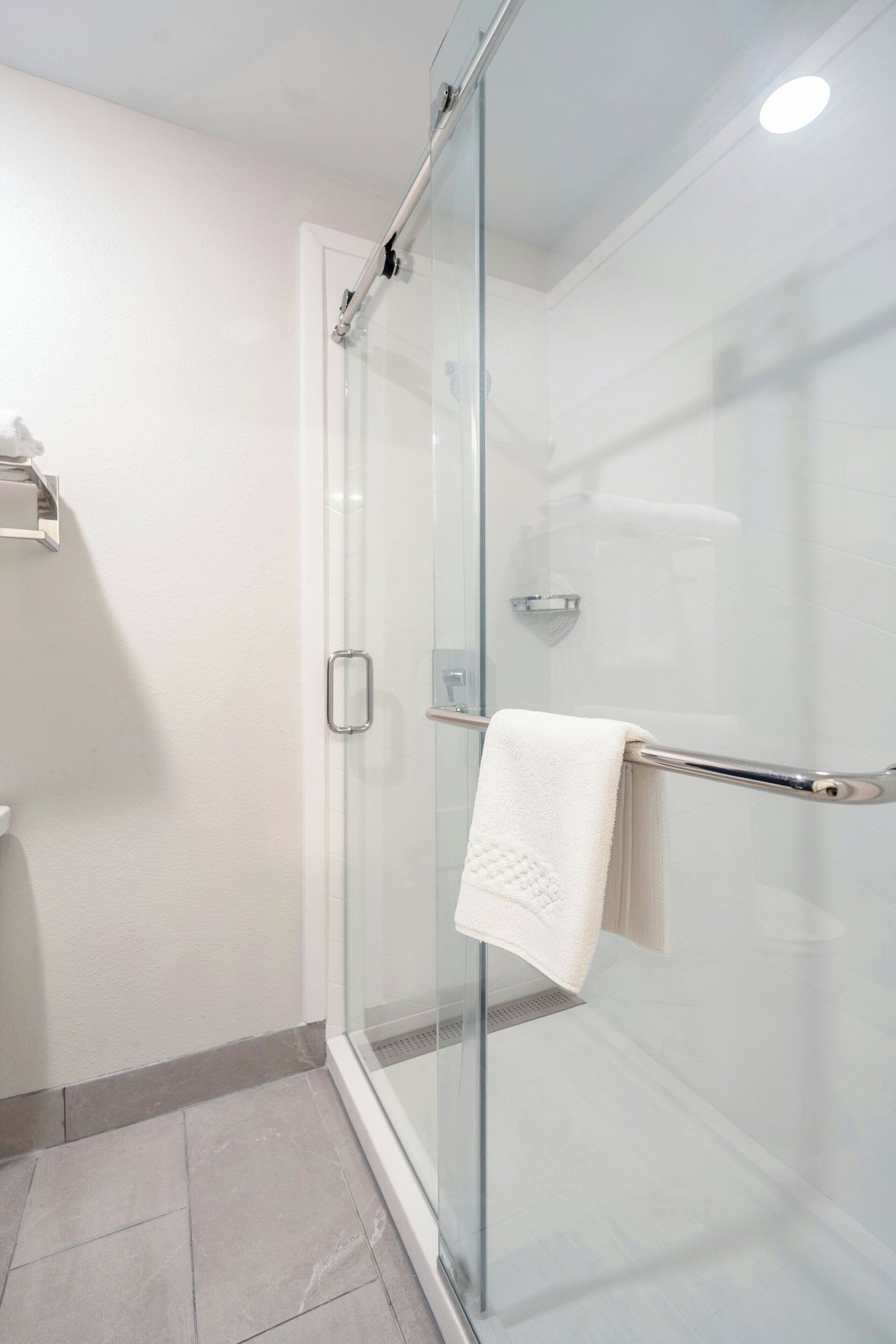 A modern bathroom with a glass shower enclosure, a white towel on a metal towel rack, and a white toilet.