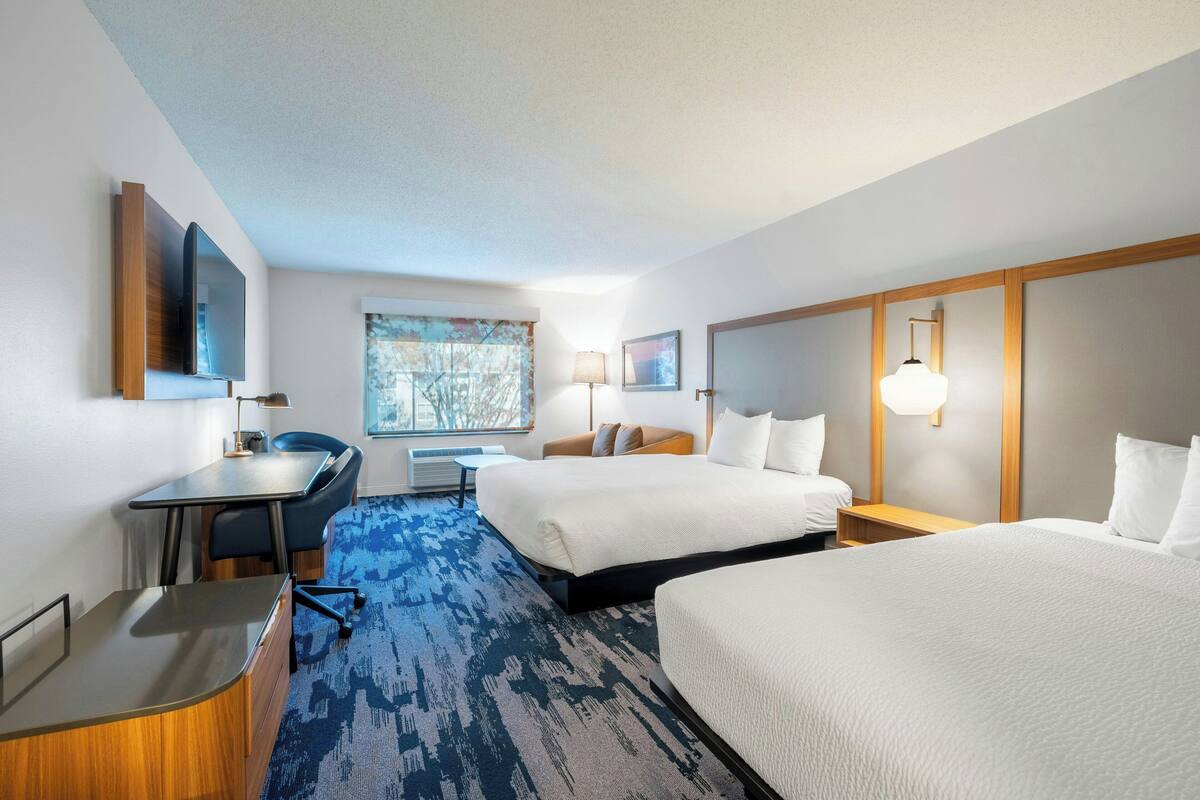 A hotel room with two beds, a desk, a chair, a TV, and a window with a view.