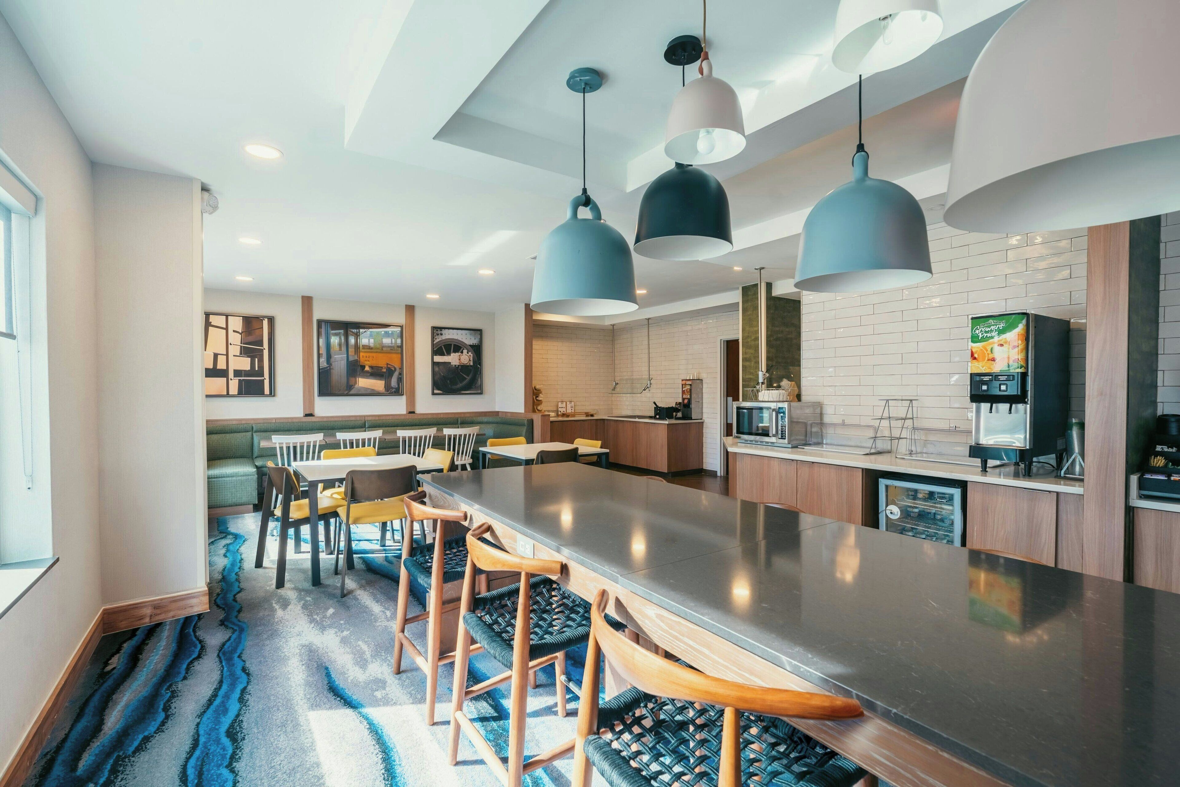 A modern kitchen with a central island, pendant lighting, and a dining area with chairs and a table.