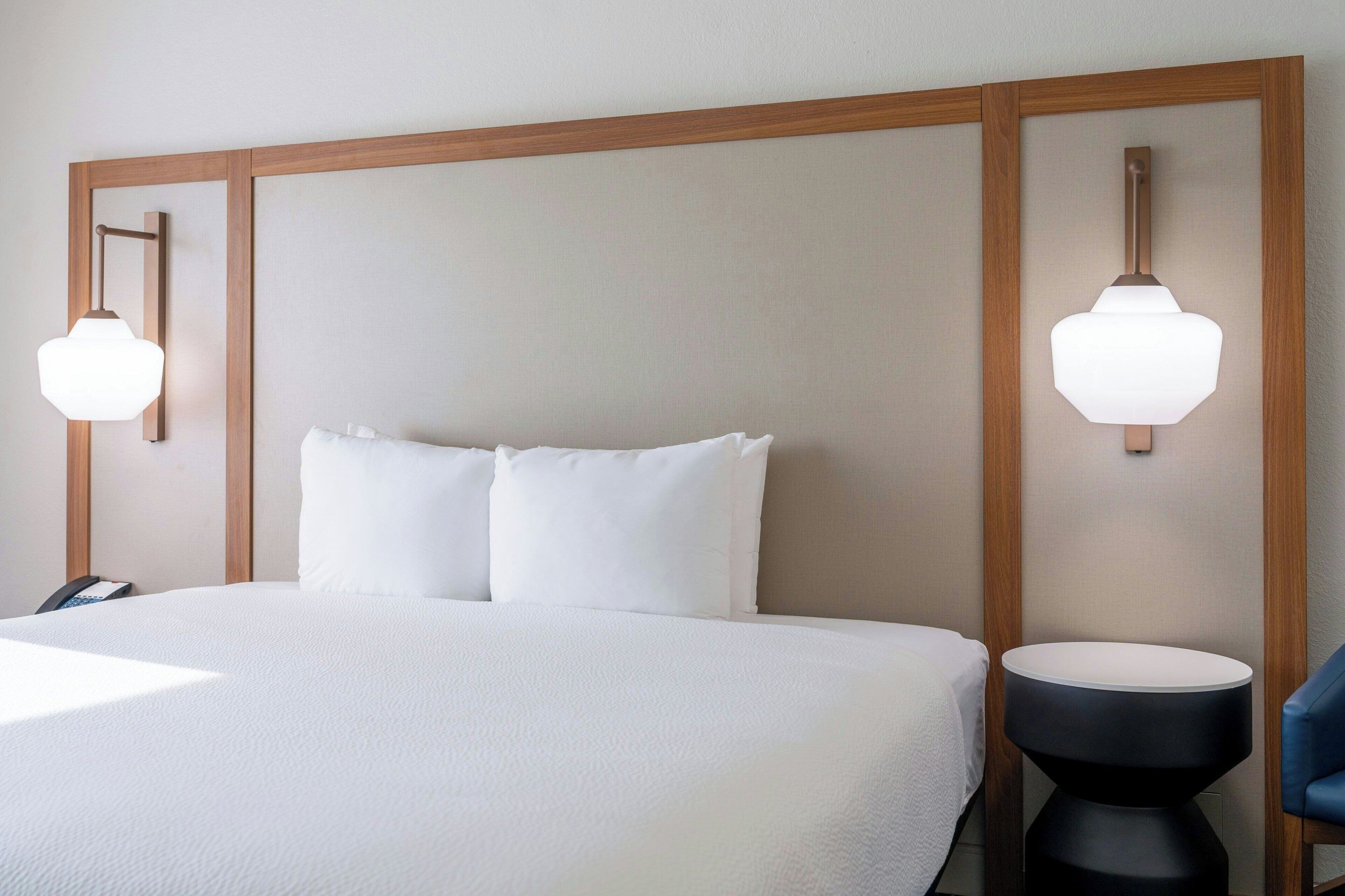 Una habitación de hotel con una cama grande, dos mesitas de noche y lámparas fijadas a la pared.