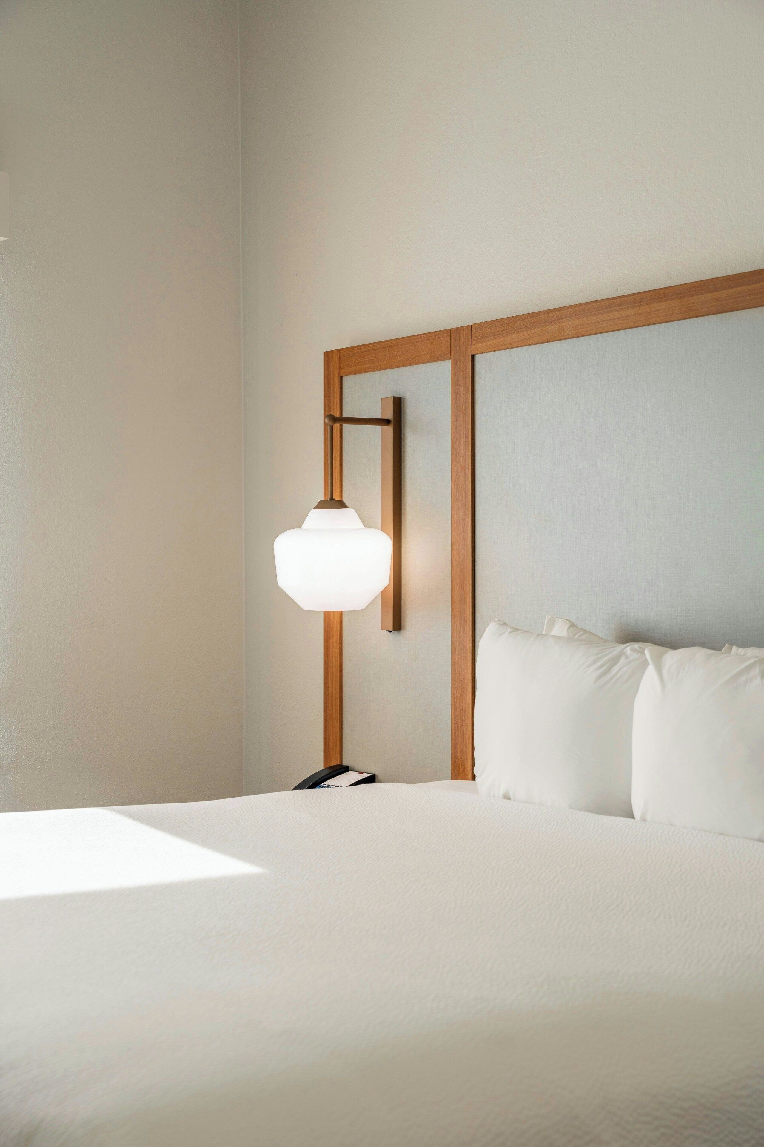 Une chambre d’hôtel avec un lit, une tête de lit en bois et une lampe fixée au mur.